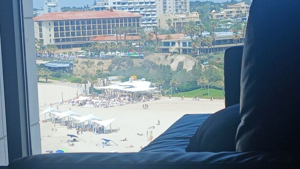 A hotel room with a view of a beach, a large window, and a bed.