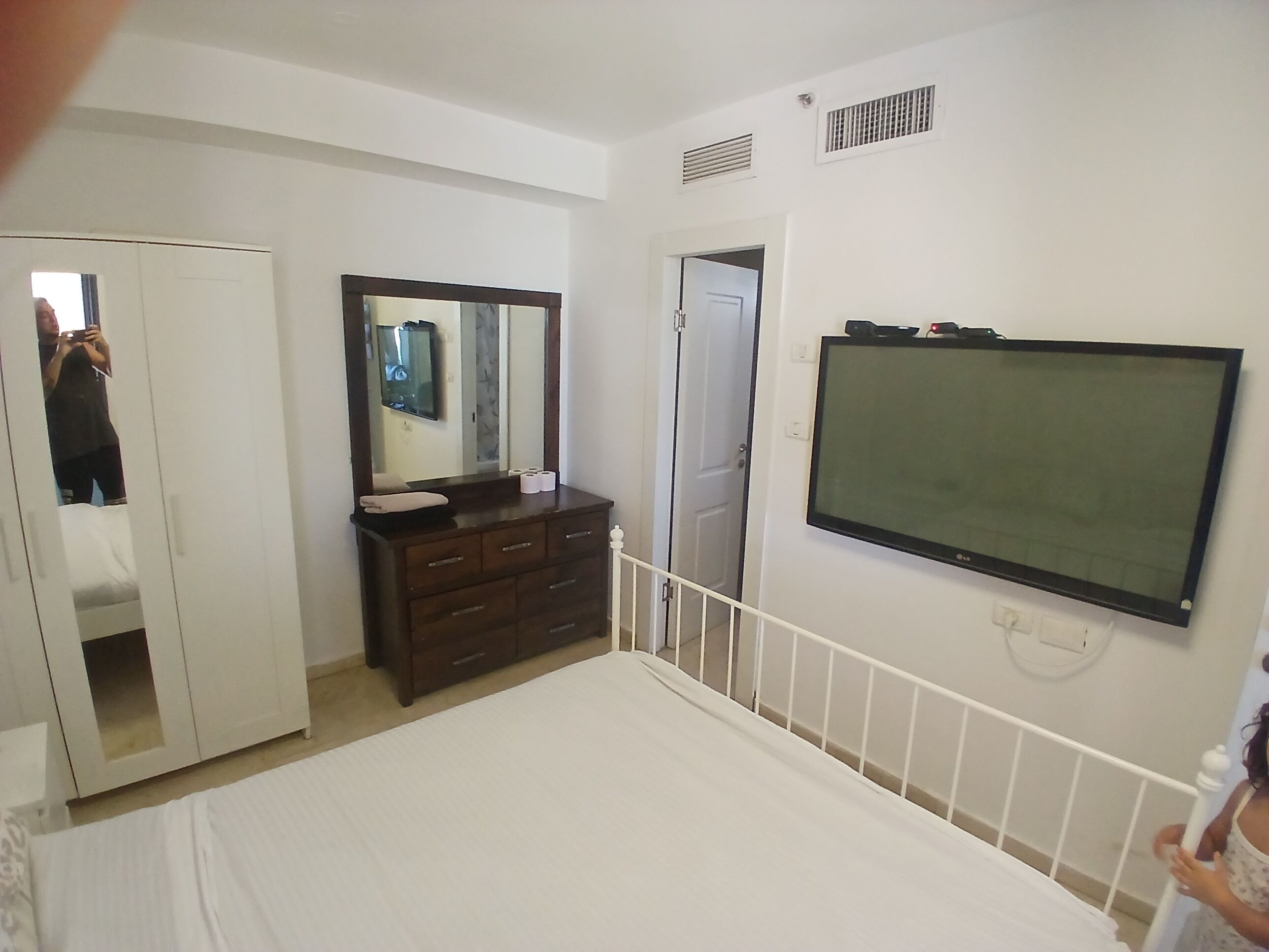 Een slaapkamer met een bed, een dressoir, een spiegel, een televisie en een kledingkast.