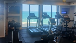 A gym with treadmills, exercise bikes, and weights, overlooking a beach.