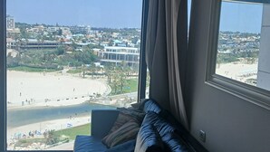 A room with a large window overlooking a beach and cityscape.