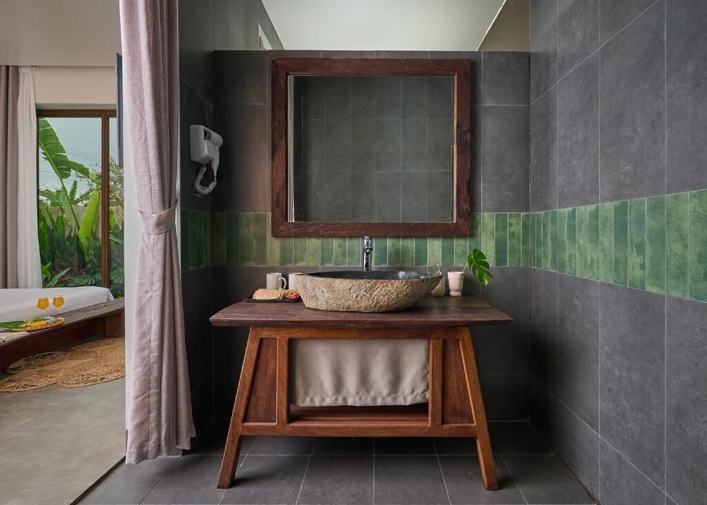 A bathroom with a round stone sink, wooden vanity, and a large mirror.