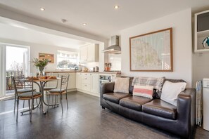 A modern living room with a leather sofa, dining table, and chairs, a kitchen in the background, and a large map on the wall. - 1 Bed in Whitby (oc-r566) (Robin Hood's Bay)