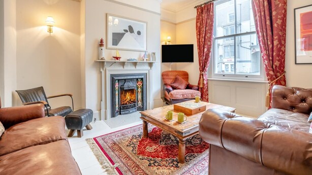 A living room with a fireplace, leather sofas, a coffee table, and a television. - 4 Bed in Whitby (oc-w919) (Whitby)
