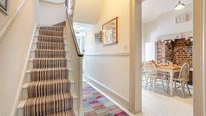 A staircase with striped carpet, a colorful rug, a dining area with a brick wall, and a white table with chairs. - 4 Bed in Whitby (oc-w919) (Whitby)