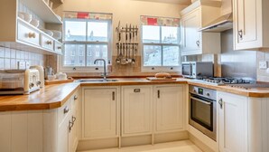 A kitchen with white cabinets, a wooden countertop, a stove, a microwave, and a window with a view of buildings. - 4 Bed in Whitby (oc-w919) (Whitby)