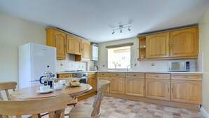 Une cuisine avec des meubles de rangement en bois, un réfrigérateur blanc, une cuisinière, un four à micro-ondes et une table à manger avec des chaises.