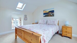 Une chambre à coucher avec un lit en bois, une table de chevet, une lampe, un tableau et une lucarne.
