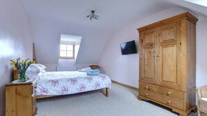 Une chambre à coucher avec un lit, une armoire en bois, une petite table avec des fleurs, un radiateur et un téléviseur fixé au mur.