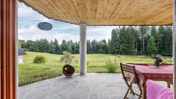 Un patio techado con suelo de piedra, una mesa de madera con mantel rosa, una silla y una lámpara colgante.