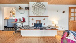 Una habitación acogedora con una zona de estar central, una cocina al fondo y techo de madera.