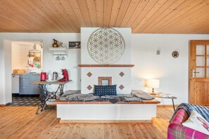 Une pièce chaleureuse avec un espace salon central, une cuisine à l’arrière-plan et un plafond en bois.