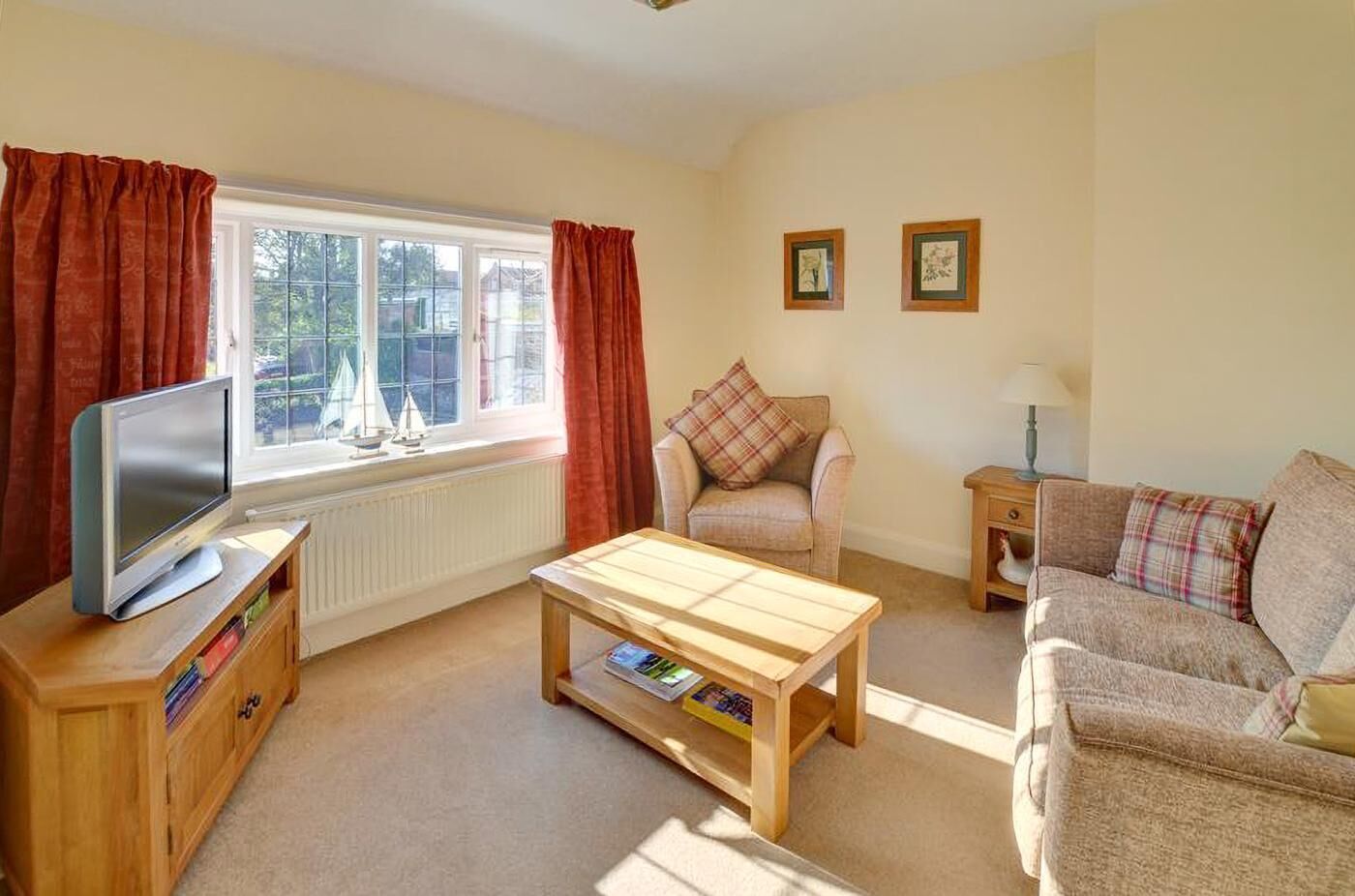 A living room with a television, a wooden coffee table, a sofa, a chair, and a window with curtains.