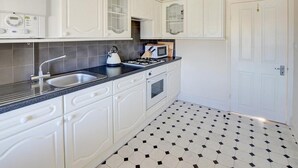 Una cocina con armarios blancos, encimera negra, hervidor, microondas y estufa.