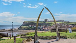Un pueblo costero con un arco monumental destacado, bancos y vista de un edificio histórico en una colina.