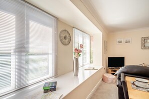A living room with a sofa, a TV, a window with blinds, a clock, and a vase with flowers. - 1 Bed in Whitby (oc-w815) (Whitby)