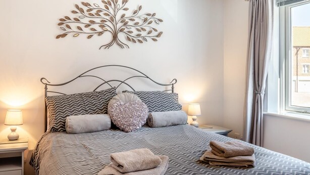Una cama bien hecha con ropa de cama estampada, un adorno en la pared y una ventana con cortinas.