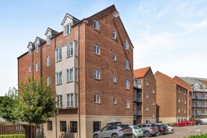 A multi-story residential building with a brick facade, multiple windows, and a parking area with cars. - 1 Bed in Whitby (oc-w815) (Whitby)
