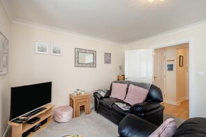 A living room with a flat-screen TV, a leather sofa, a small wooden side table, and a pink pouf. - 1 Bed in Whitby (oc-w815) (Whitby)