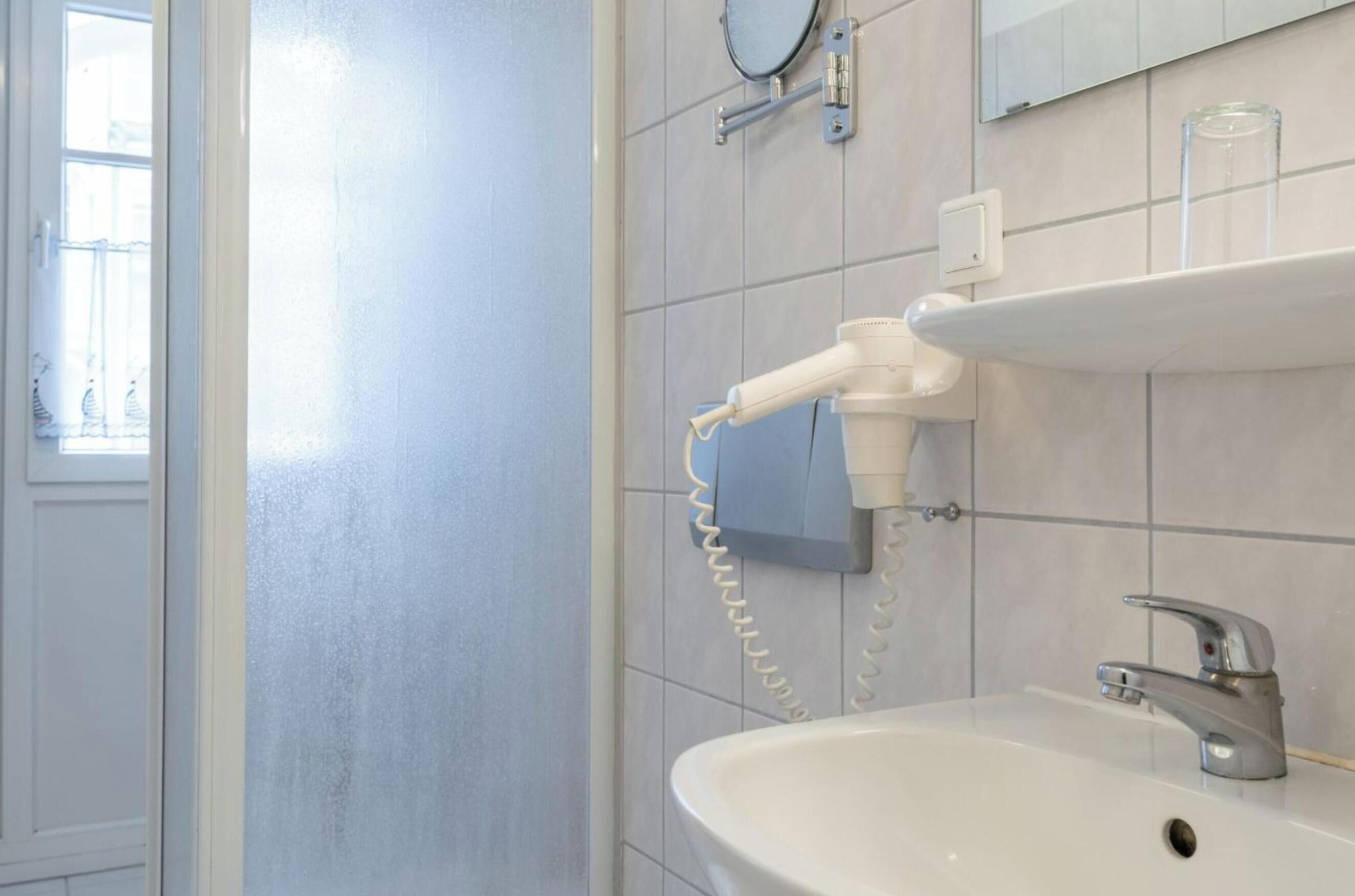 Een badkamer met een witte wastafel, een spiegel, een haardroger en een raam met uitzicht op een balkon.