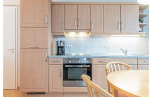 A kitchen with wooden cabinets, a built-in oven, a coffee maker, and a dining table with chairs.