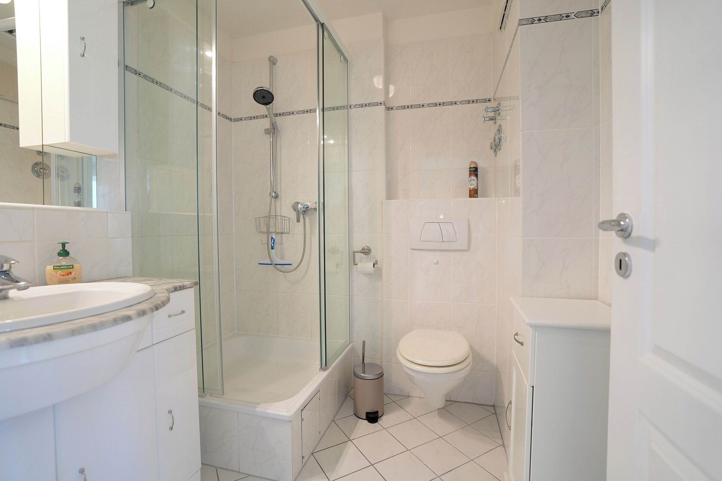 Une salle de bain dotée d’une douche à parois de verre, de toilettes blanches et d’un lavabo avec un plan de travail en marbre.