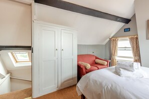 Une chambre d’hôtel avec un lit, un fauteuil rouge, une armoire et une lucarne.