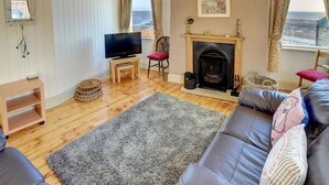 A cozy living room with a fireplace, a television, and a view of the sea. - 1 Bed in Whitby (oc-r049) (Robin Hood's Bay)