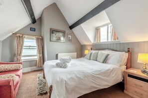 A bedroom with a bed, a nightstand, a window with curtains, a radiator, and a view of the sea. - 1 Bed in Whitby (oc-r049) (Robin Hood's Bay)