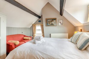 A hotel room with a bed, a red sofa, a radiator, and two framed pictures on the wall. - 1 Bed in Whitby (oc-r049) (Robin Hood's Bay)