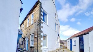 A narrow street with a white building featuring a stone facade and a blue door. - 1 Bed in Whitby (oc-r049) (Robin Hood's Bay)