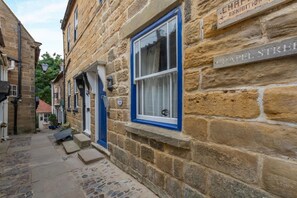Une rue étroite pavée, bordée de bâtiments des deux côtés, un ciel dégagé et une enseigne bien visible indiquant « CHAPEL STREET ».