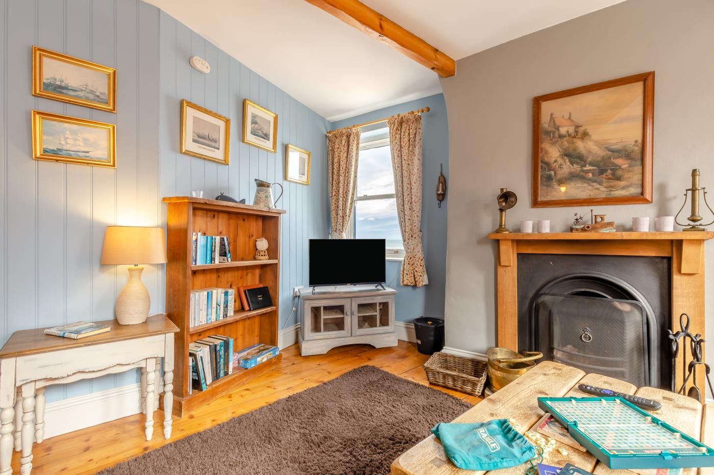 A cozy living room with a fireplace, bookshelves, a television, and a window with curtains.