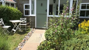 A stone building with a green door, a covered porch, and a garden with plants and a pathway. - 2 Bed in Sleights (oc-wa228a) (Sleights)