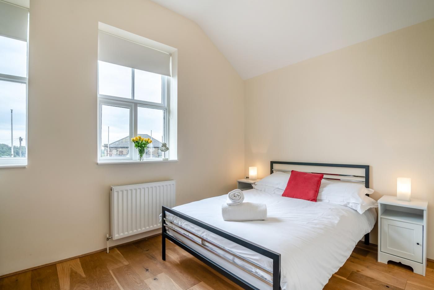 A bedroom with a bed, two bedside tables, a window with a view, and a radiator.
