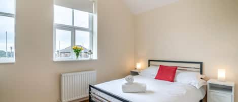 A bedroom with a bed, two bedside tables, a window with a view, and a radiator.