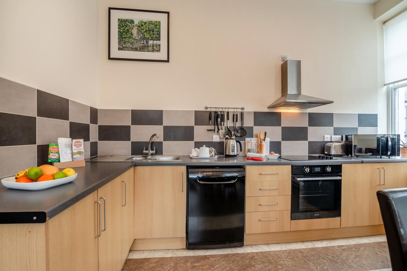 A modern kitchen with a black dishwasher, stainless steel appliances, and a checkered tile backsplash.