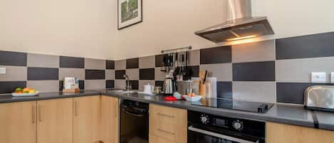 A modern kitchen with a black and gray tile backsplash, stainless steel appliances, and wooden cabinets.