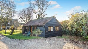 A small, dark-colored wooden house with a sloped roof, a front porch, and a gravel driveway. - 1 Bed in Great Waldingfield (oc-n33972) (Great Waldingfield)