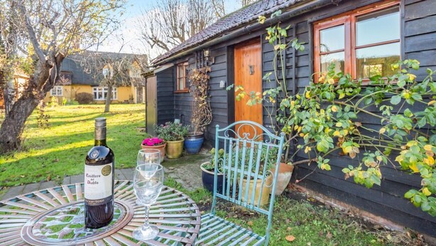 A rustic wooden house with a garden, a metal table with a bottle and glasses, and potted plants. - 1 Bed in Great Waldingfield (oc-n33972) (Great Waldingfield)