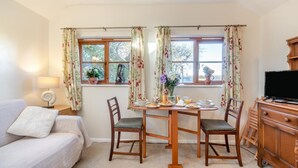 A cozy room with a dining table set for breakfast, a sofa, and a TV on a wooden cabinet. - 1 Bed in Great Waldingfield (oc-n33972) (Great Waldingfield)