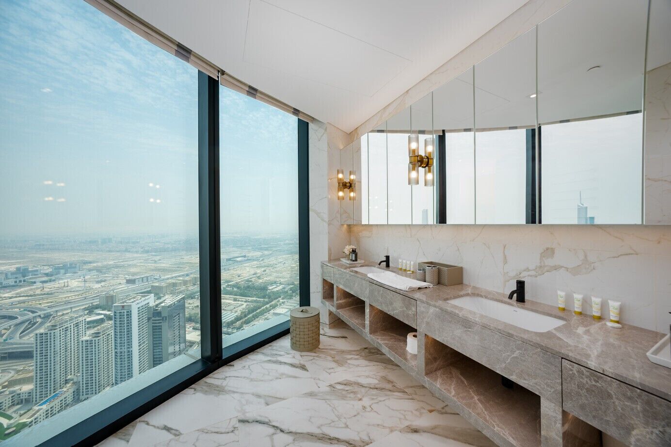 Een hotelbadkamer op een hoog etage met een groot raam, een marmeren wastafel en uitzicht over de stad.