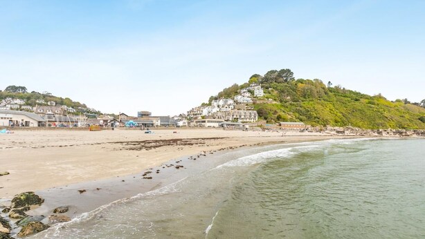 A coastal beach with buildings on a hillside, clear skies, and calm sea. - 2 Bed in Looe (oc-l10094) (Looe)
