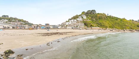 A coastal beach with buildings on a hillside, clear skies, and calm sea.