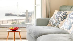 A living room with a sofa, a small table with a bowl of fruit, and a view of a dock and water. - 2 Bed in Looe (oc-l10094) (Looe)