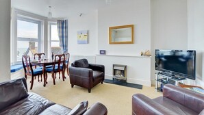 A living room with a fireplace, a television, and a dining area with chairs and a table. - 1 Bed in Looe (oc-l30006) (Looe)