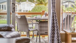 Varanda com mobiliário de vime, uma mesa com uma bandeja de objetos e vista para um edifício branco e vegetação.