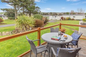 Eine Terrasse mit Korbstühlen und einem Tisch, mit Blick auf eine Rasenfläche und Mobilheime.