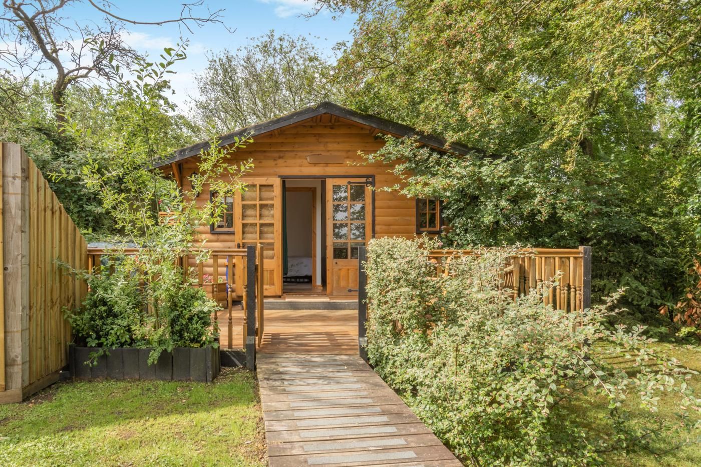Une cabane en bois dotée d’une terrasse en bois menant à l’entrée, le tout entouré d’une végétation luxuriante.