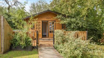 Une cabane en bois dotée d’une terrasse en bois menant à l’entrée, le tout entouré d’une végétation luxuriante.