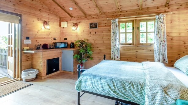 Une cabane en bois avec un lit, une petite cuisine et une fenêtre avec des rideaux.